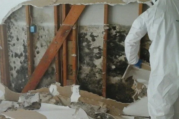 A man in a white coat stands in a burned home, assessing the damage caused by the fire.