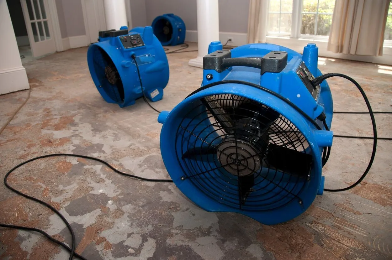 Several Large Blue Air Blowers Being Used In A Room With Damaged Flooring